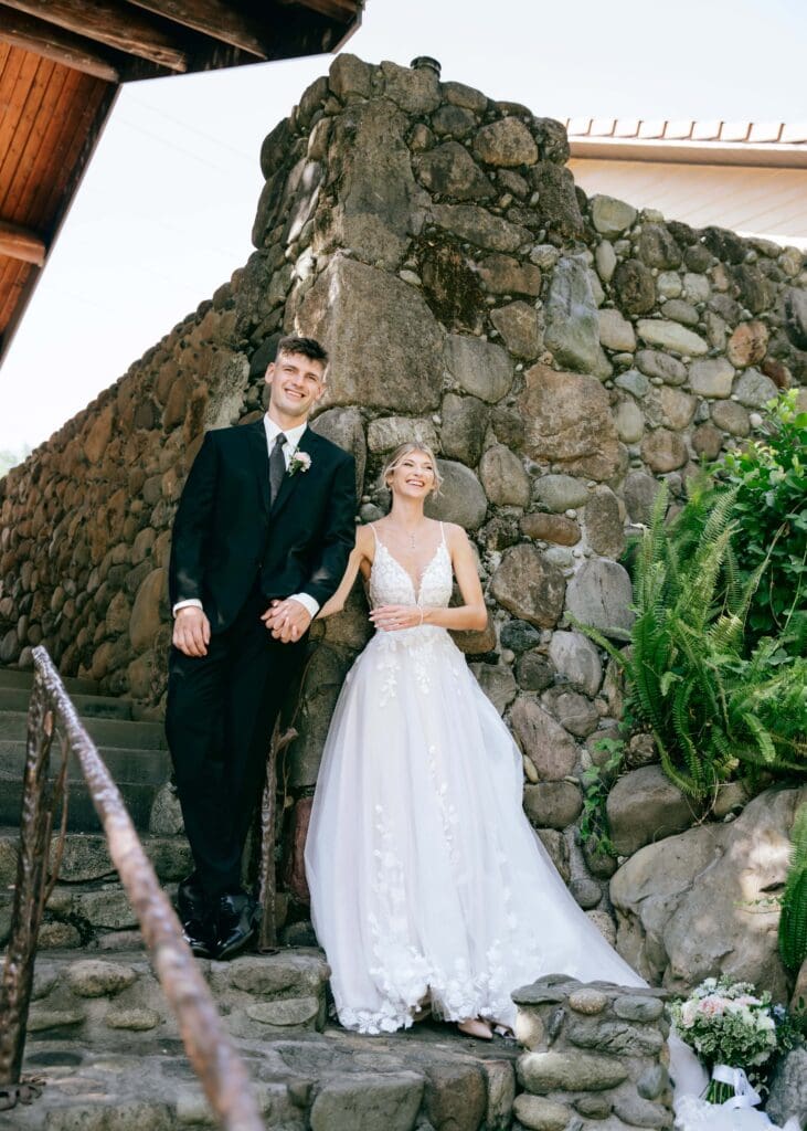 Bride and groom holding hands and leaning against a stone wall at Centerville Estates during their first touch