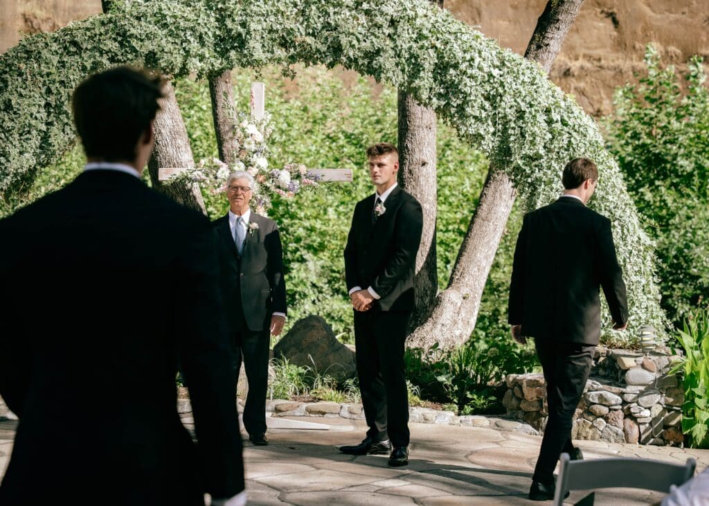 Groom standing at the alter while his groomsmen walk down the aisle during outdoor wedding ceremony at Centerville Estates