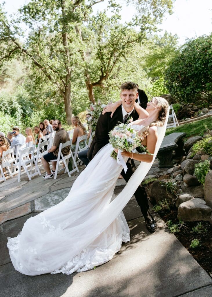 Groom dips his bride at the end of the aisle after their elegant outdoor wedding ceremony at Centerville Estates