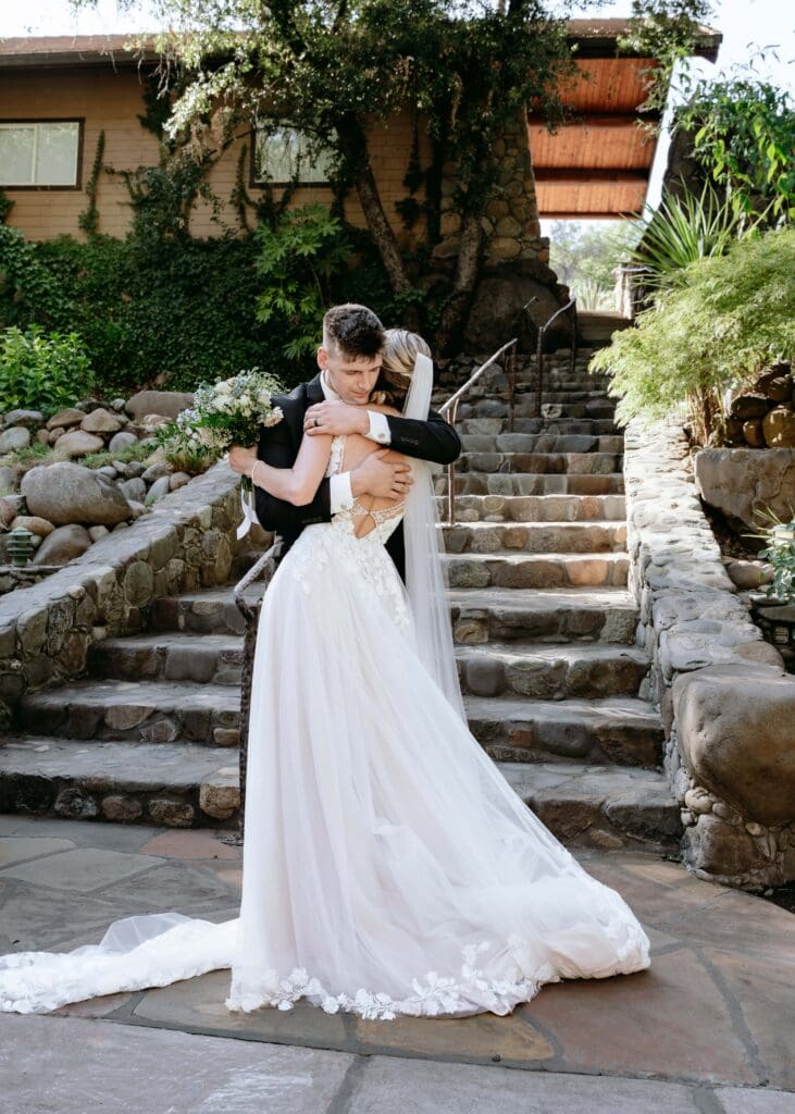 Groom hugging bride tight at the bottom of a stone staircase after the outdoor wedding ceremony in Northern California