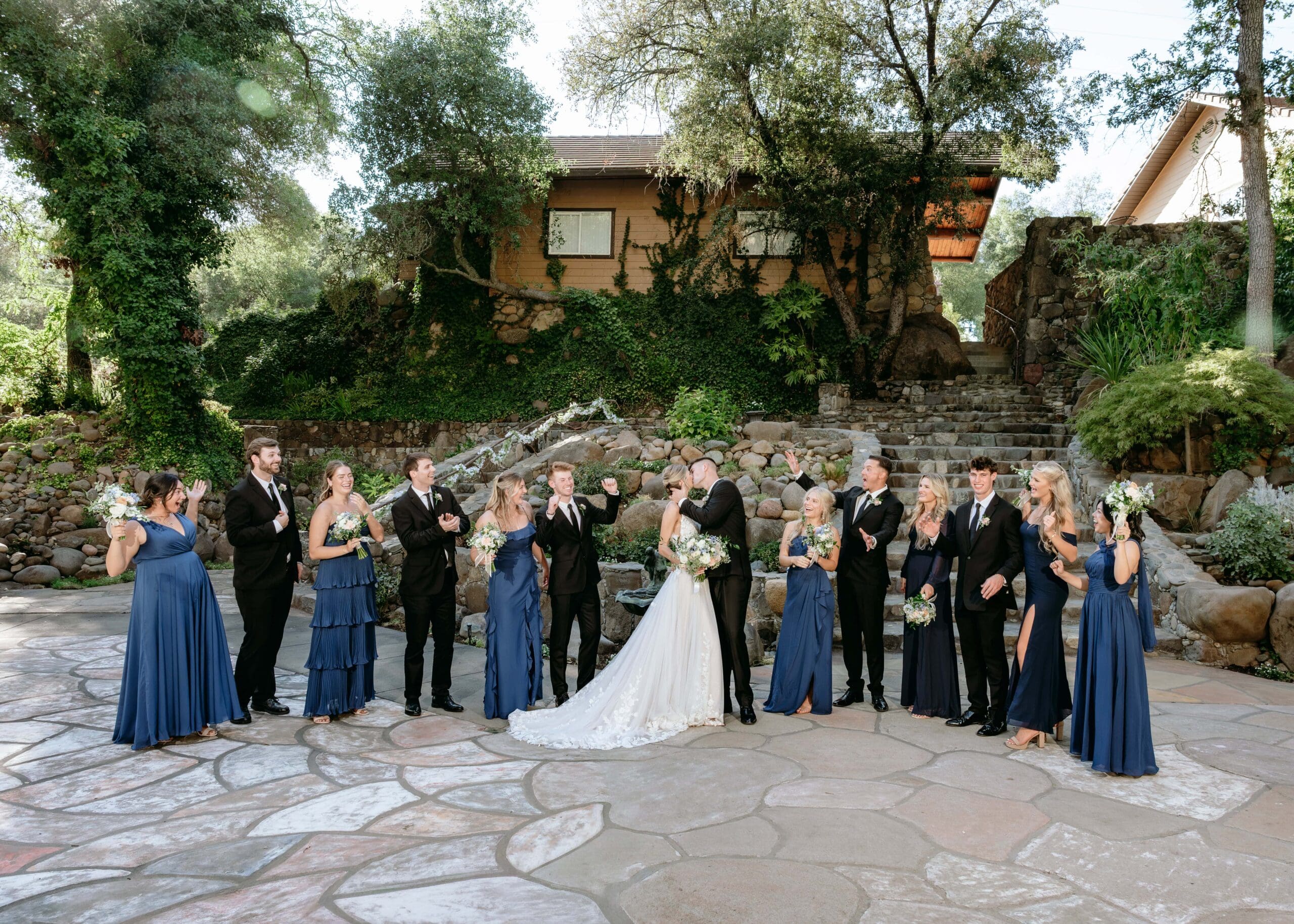 Wide shot of the full bridal party cheering as the bride and groom kiss in the middle at Centerville Estates