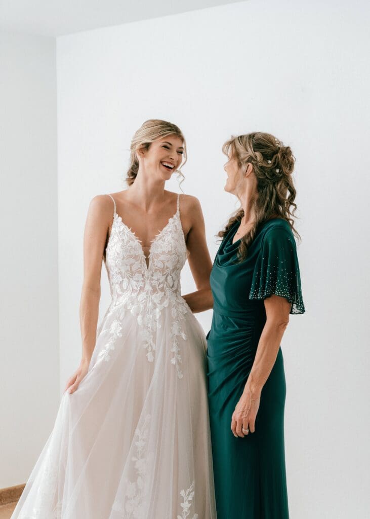 Getting ready moment of the Mother of the bride and bride smiling at each other in a white room