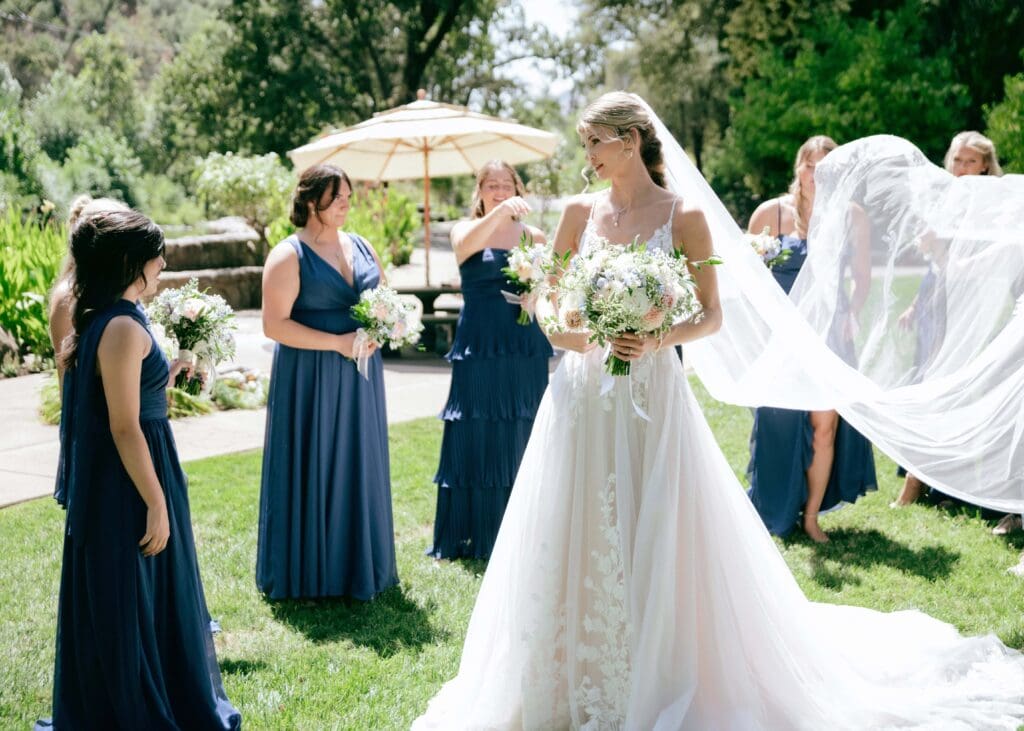 bridesmaids stand around the bride holding bouquet as one of them fluffs her veil