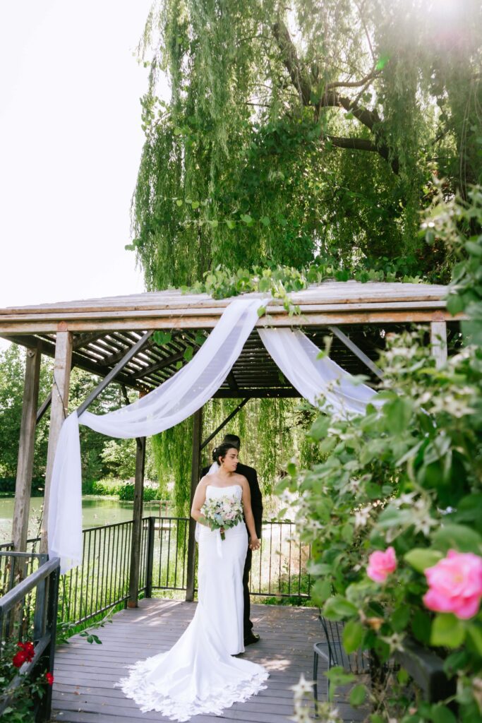wedding day first touch as the bride and groom stand back to back under a pond-side gazebo