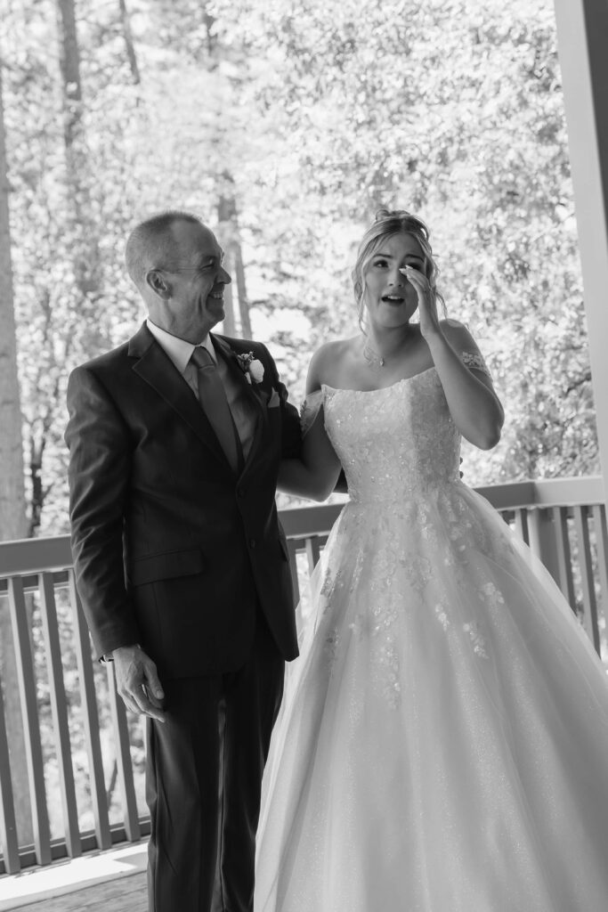 Bride wiping tears away with her arm around her father as he smiles at her after seeing her for the first time