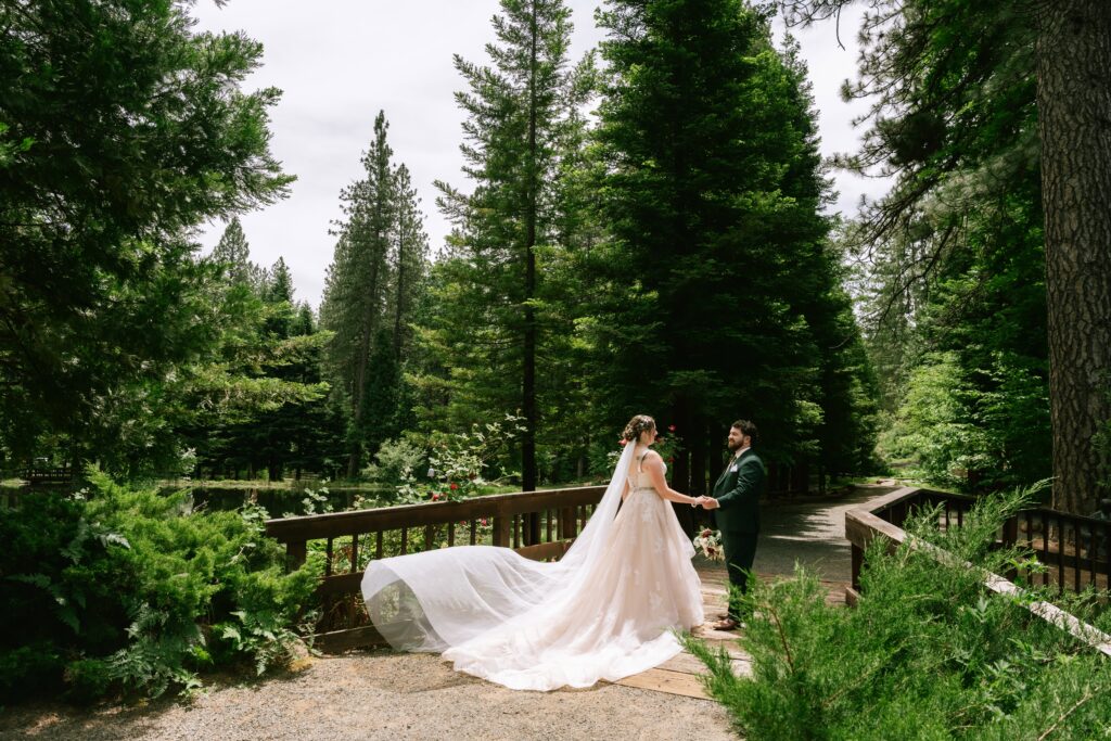 Bride and groom facing each other on a bridge surrounded by tall green trees at Clotilde Merlo Park